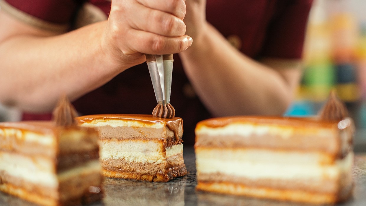Mujer dando detalles finales a tartas con manga de chocolate.