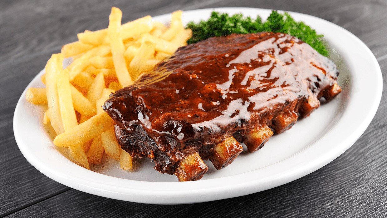 Plato de costillas de cerdo con papas fritas y ensalada.