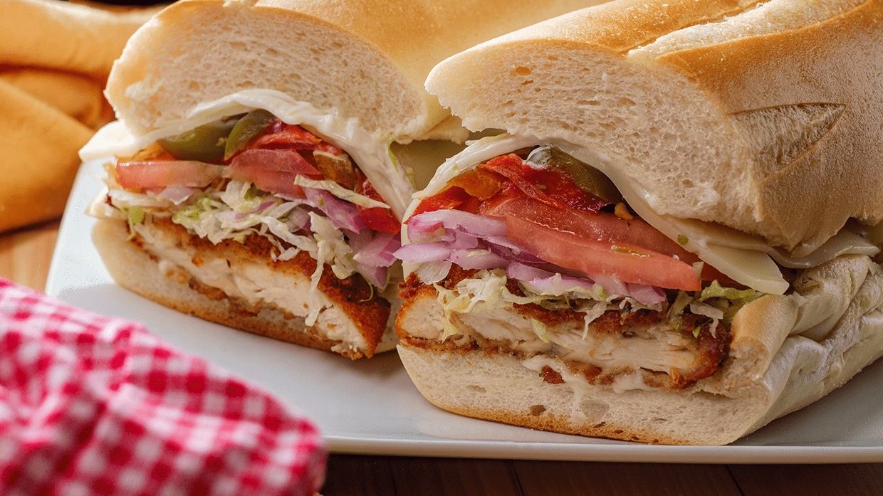 Sandwich de milanesa partido en mitades con tomate y lechuga.