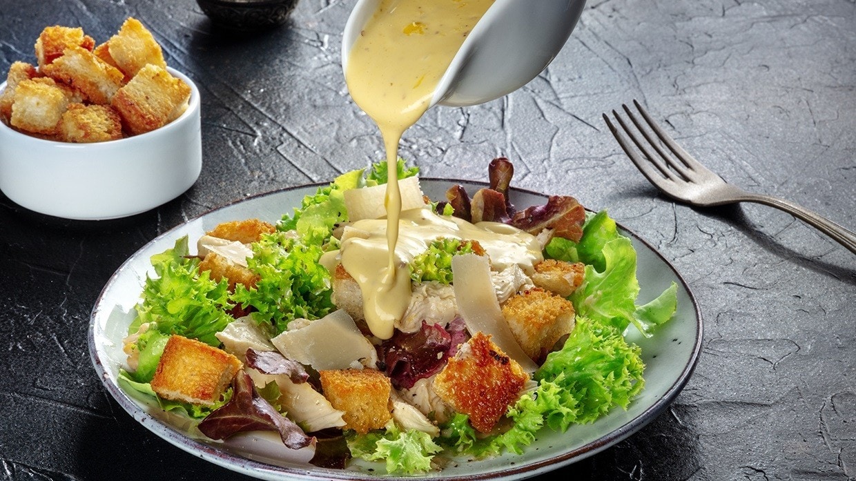 Plato de ensalada caesar siendo servido con aderezo